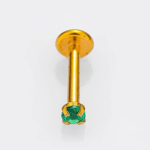 Dettaglio macro di un piercing in titanio dorato con zircone verde incastonato a quattro griffe