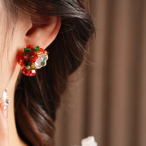 Close-up of handmade beaded floral earrings with red and green glass seed beads on a model