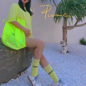 Detail view of vibrant neon yellow mesh tote bag and matching socks in a summer outdoor setting