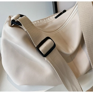 Detail of off-white nylon crossbody bag featuring a wide strap and black adjustable buckle