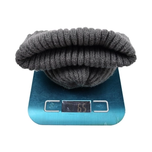 Thick grey knitted beanie hat with rolled edge showing 65g weight on a scale