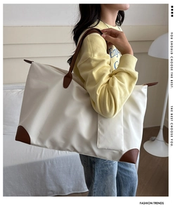 Detail view of large cream oxford tote bag with brown leather handles and side text
