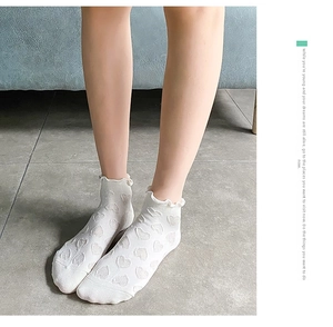Detailed view of white cotton socks with heart jacquard patterns and ruffled edges