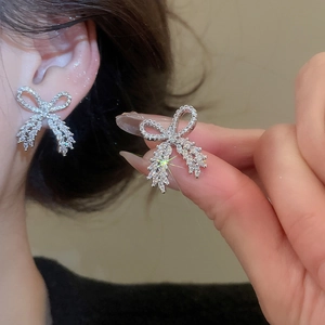 Macro detail of silver bow earrings with sparkling cubic zirconia on model's ear