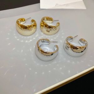 Detailed view of gold and silver C-shaped earrings featuring a hammered metal texture