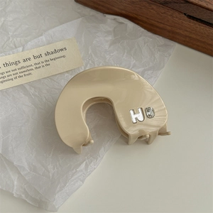 Detail of beige acrylic claw clip featuring inlaid H letter and sparkling diamond decoration