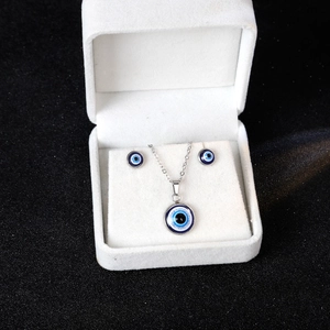 Detailed view of evil eye necklace and stud earrings set in a white velvet jewelry box