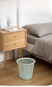 Detail of mint green hollow mesh plastic wastebasket on wooden floor in bedroom