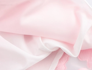 Detailed macro view of soft pink and white floral jacquard fabric with scalloped edge trim