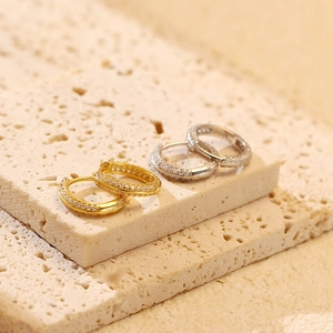 Detail of silver and gold paved zircon hoop earrings on a textured stone surface