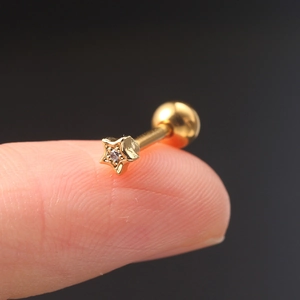 Macro detail of a gold star cartilage stud with zircon inlay held on a fingertip