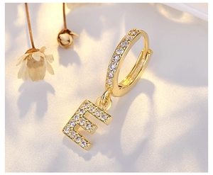 Macro shot of gold letter E earring with sparkling crystals on white fabric background