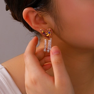 Elegant gold heart earrings with pink and blue stones and long pearl tassels on a model