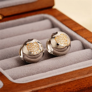 Detail of silver twisted huggie earrings with gold heart zircon in a premium jewelry box