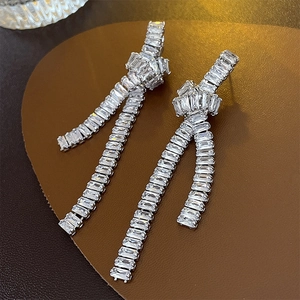 Close-up of silver tassel earrings with knot design and sparkling zircon stones