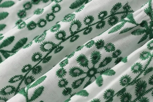 Detailansicht der weißen Stickerei mit grünen Blättern und Lochmuster auf dem Kleid