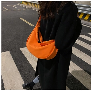 Close-up of bright orange nylon dumpling bag with black zipper on model wearing black coat