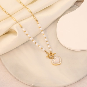 Golden heart pendant necklace with pearls and t-bar clasp on white marble surface