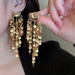 Close-up of golden U-shaped tassel earrings with clusters of round sequins on a model