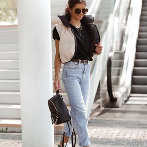 Outdoor street style view of beige cropped puffer vest paired with blue jeans and backpack