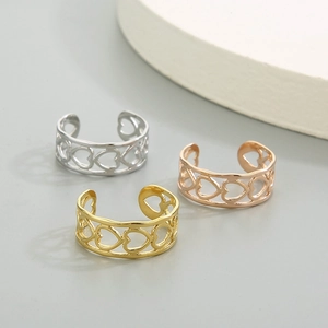Trois bagues cœur évidées en argent, or et or rose sur un fond gris neutre