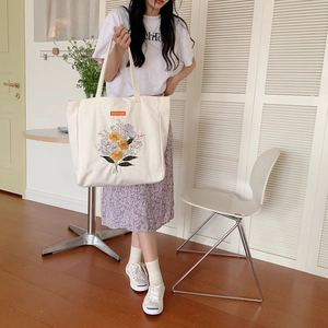 Detailed embroidery of colorful flowers and orange label on a white canvas tote bag