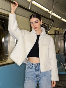 Chic white faux fur zip jacket with high collar shown in a modern urban subway setting