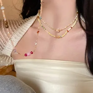 Detail view of layered gold chain necklace with colorful red and pink beaded accents