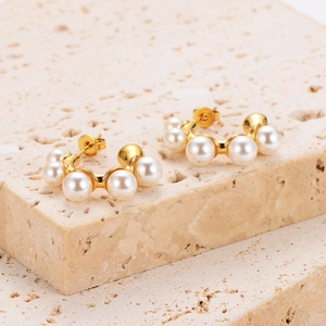 Elegant gold plated C-shaped pearl earrings displayed on a textured stone background