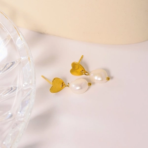 Élégantes boucles d'oreilles cœur doré avec perles blanches sur un plateau en verre