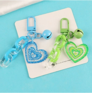Close-up of blue and green acrylic heart keychains with glitter and small metal bells