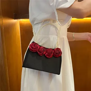Detail of elegant black satin evening bag with red silk roses and pearl bead handles