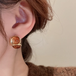 Close-up of amber resin square earring with gold metal frame worn by a model