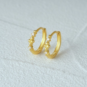 Macro detail of gold S925 sterling silver hoop earrings with white zircon flower accents