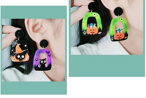 Macro shot of Halloween acrylic earrings featuring a skull, black cat, and pumpkin charms