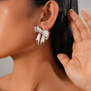 Close-up of a silver bow earring with metallic luster worn by a model on a grey background