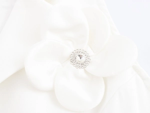 Close-up of white fabric flower detail with sparkling crystal rhinestone center on a vest
