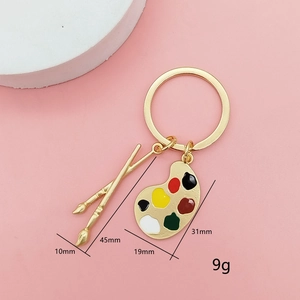 Detailed size view of gold artist palette and brushes keychain charm on pink background