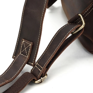 Detail of dark brown leather shoulder strap with reinforced stitching and bronze metal buckle