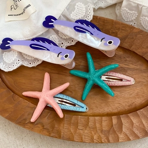 Detailed view of acrylic fish and resin starfish hair clips on a decorative wooden tray