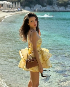 Detail of yellow floral tiered lace dress and brown leather handbag on beach