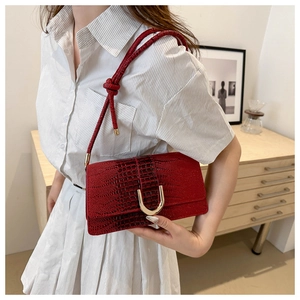 Detail of red crocodile pattern bag featuring a golden U-shaped buckle and woven strap