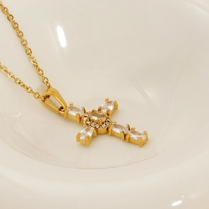 Macro shot of gold cross necklace with oval-cut cubic zirconia in a white ceramic bowl