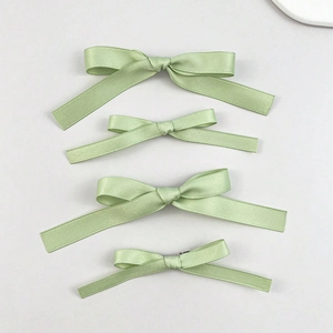 Detailed view of four light green satin ribbon hair bows with silky texture and fine sheen