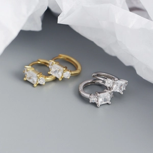 Macro shot of gold and silver S925 square zircon hoop earrings on pleated paper