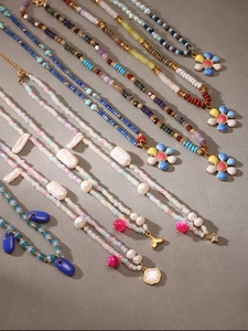 Detail of beaded necklaces with enamel flower charms and colorful glass beads on sand