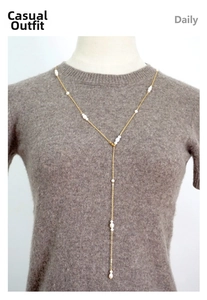 Detailed view of a long gold-tone Y-necklace with elegant freshwater pearls on a sweater