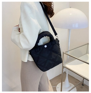 Detail of black quilted nylon bucket bag with white button and adjustable strap