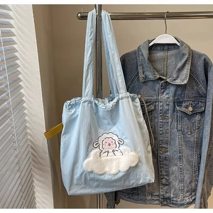 Detail of light blue tote bag featuring cartoon sheep patch embroidery on a canvas surface