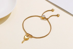 Détail du bracelet en titane doré avec breloque clé-cœur et chaîne ajustable à perles